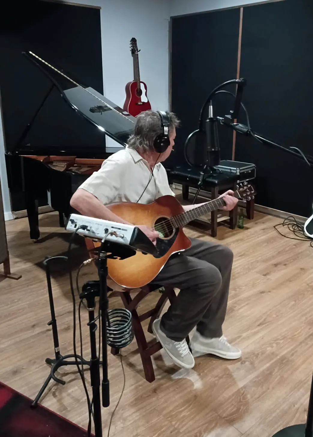 Singer-songwriter recording acoustic guitar and vocals beside Studio A’s baby grand piano